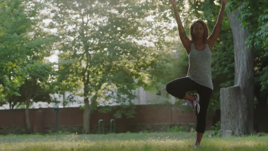 A woman is doing yoga on one leg in a park