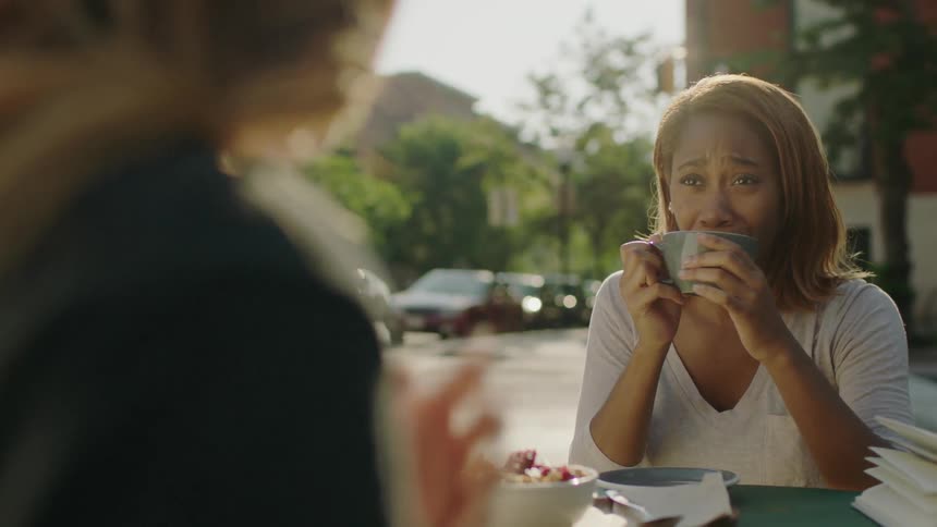 Two women are laughing and talking at a cafe table outside