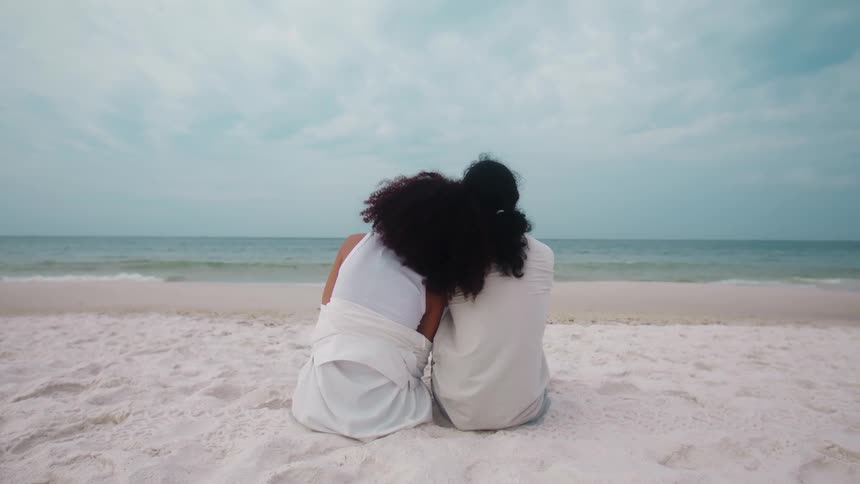 Two women are sitting on the sand together