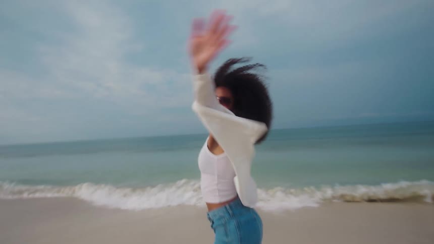 Woman with sunglasses and curly hair running on the beach