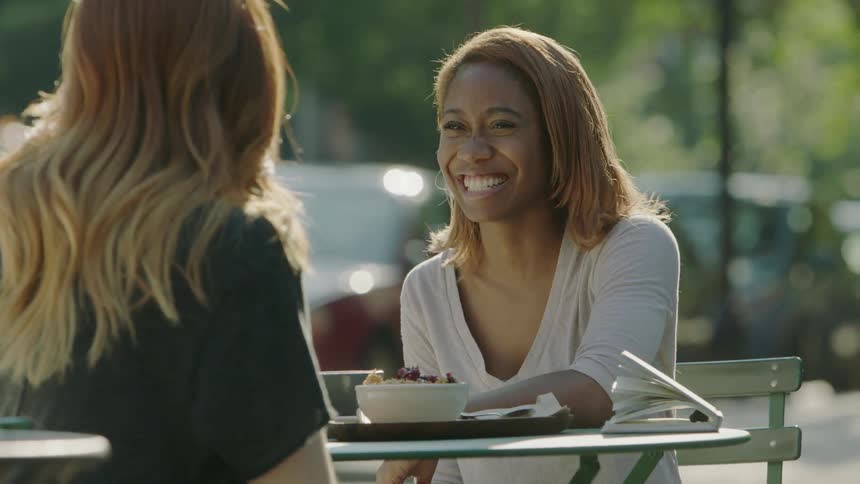 Two women are laughing and talking at a table outside
