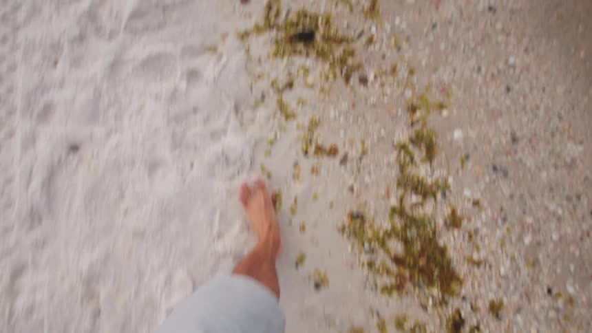 A person walks barefoot on a sandy and rocky beach