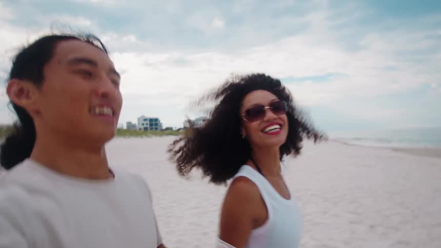 A man and a woman running on the beach toward the sea holding hands happily
