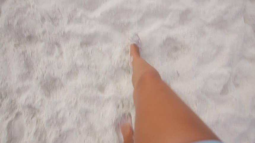 A person walks barefoot across white beach sand