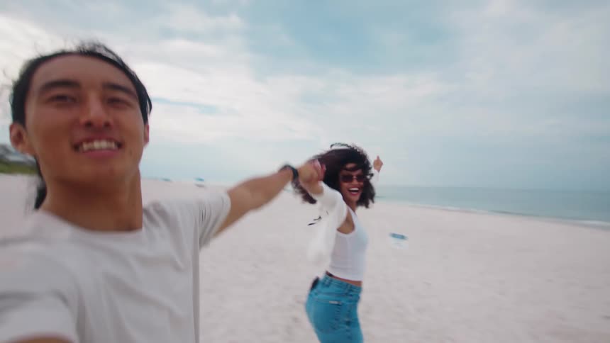 A couple having fun on the beach holding hands with the woman wearing sunglasses
