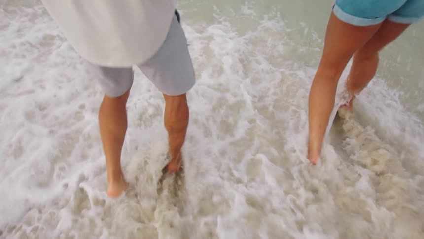 A man and woman are shown from the waist down hopping in shallow ocean water