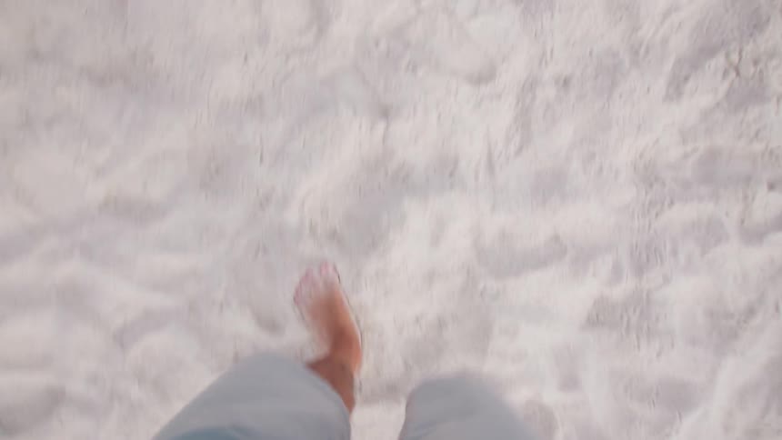 Legs of a person with shorts and barefoot walking in the sand