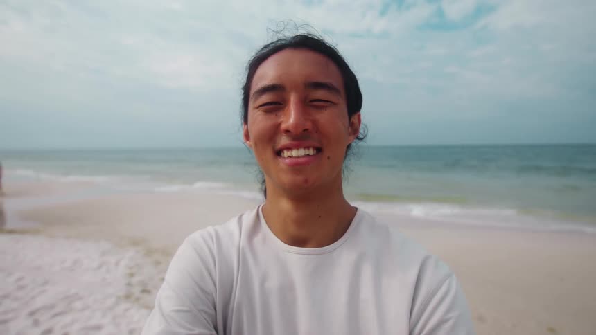 A smiling man stands on the beach near the ocean