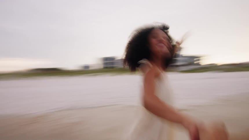 A couple is running joyfully on a beach the woman is leading and the man is following holding her hand they are running toward the camera and then the clip abruptly ends
