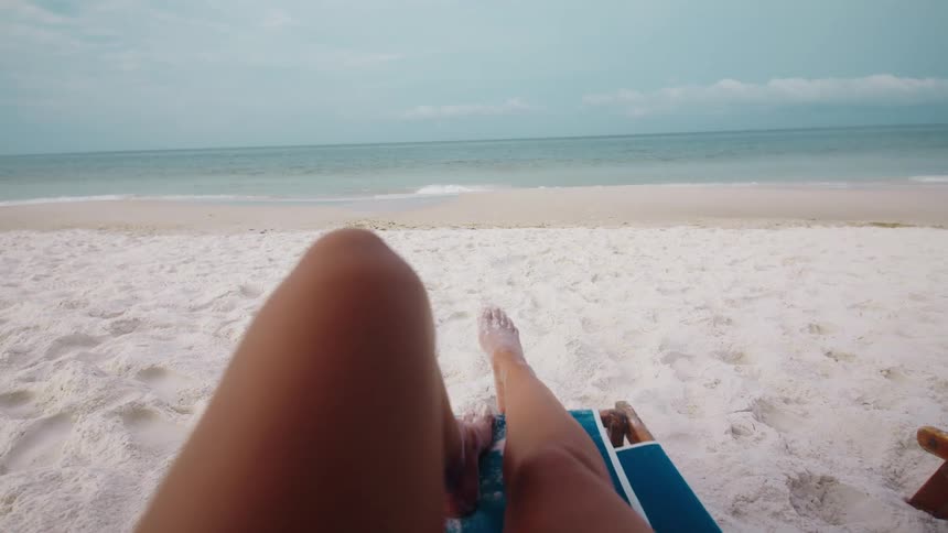 The woman is relaxing on the beach chair near the ocean