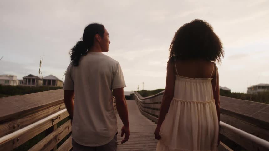 A couple walking side by side on a pedestrian bridge talking along the way