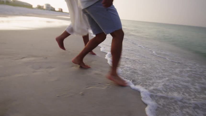 Close up of a young man and woman walking to and running away from ocean waves at the shore during daytime