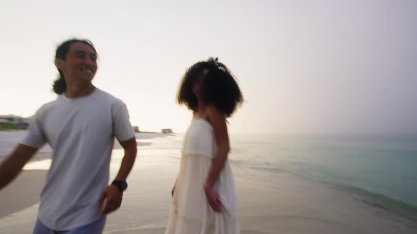 A joyful couple walks playfully along a beach during sunset