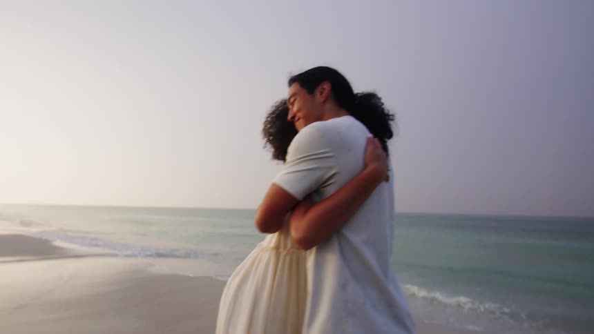 A happy couple warmly hugs each other on the beach at sunset