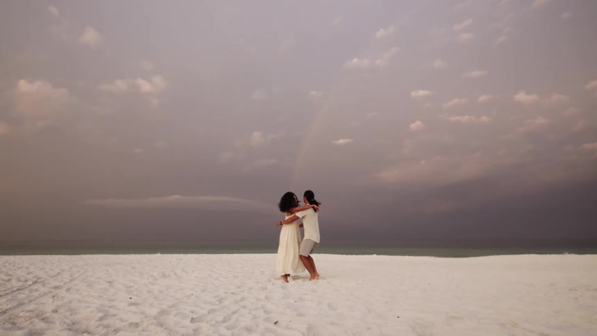 Couple embraces on a quiet beach beneath a pastel sky
