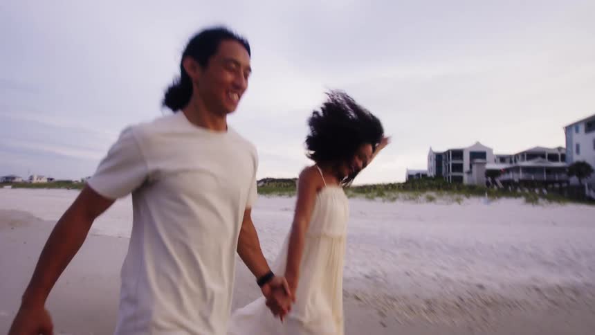 A couple hold hands and run on the beach together