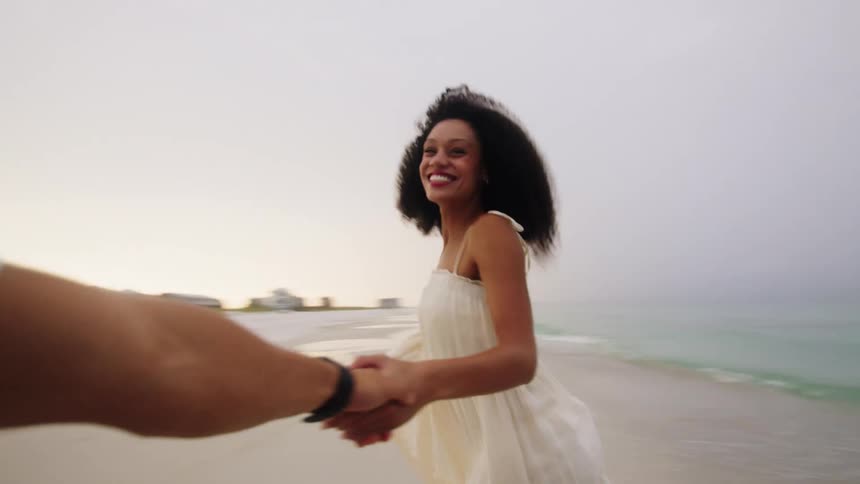 Smiling woman in a white dress spinning hand in hand with someone by the sea