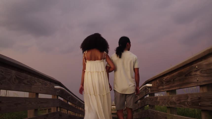 A couple walks hand in hand toward the beach at sunset