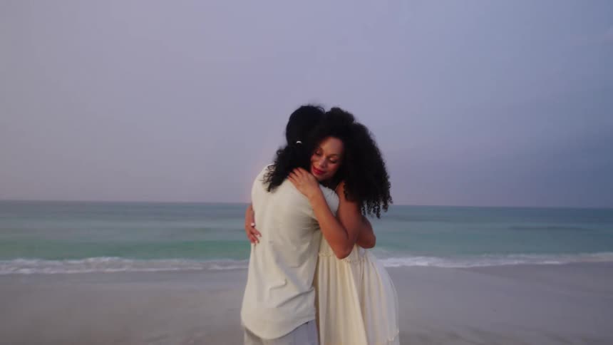 A man and a woman hugging at the edge of the beach