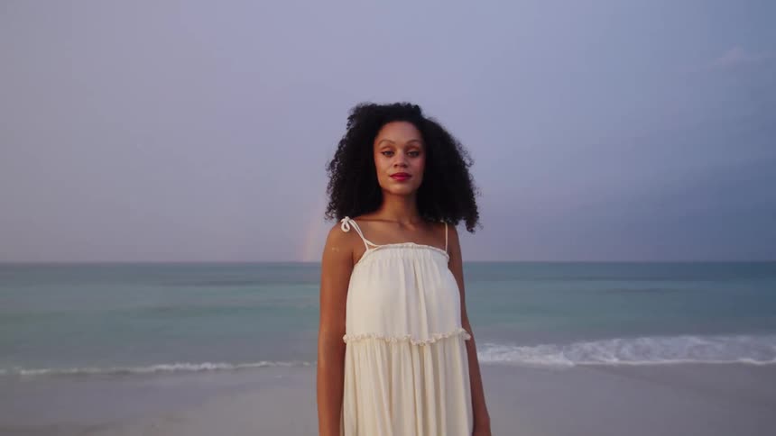 Woman stands at beach facing the camera