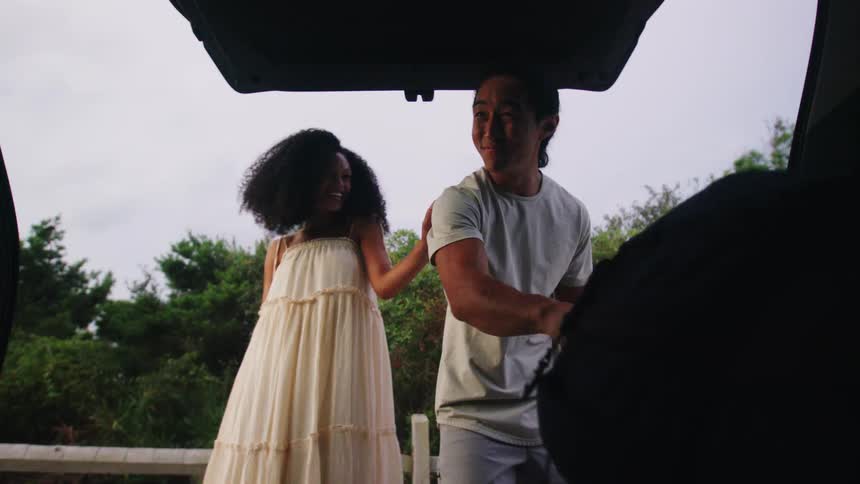 Man taking a backpack from the trunk of a car accompanied by a woman