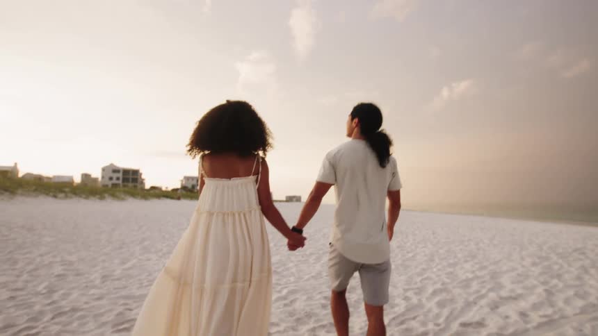 Couple walking hand in hand on the white sand beach at sunset