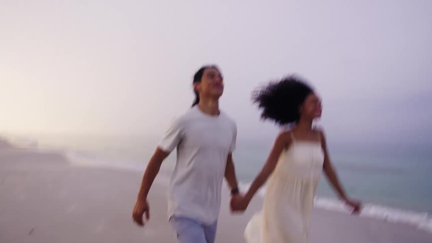 Couple running hand in hand on the beach at sunset smiling joyfully