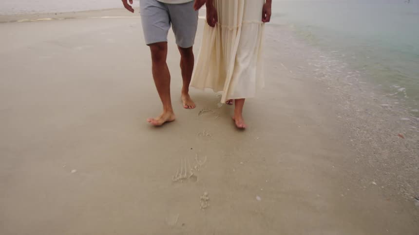 Couple walking on sandy shoreline as small waves gently roll in