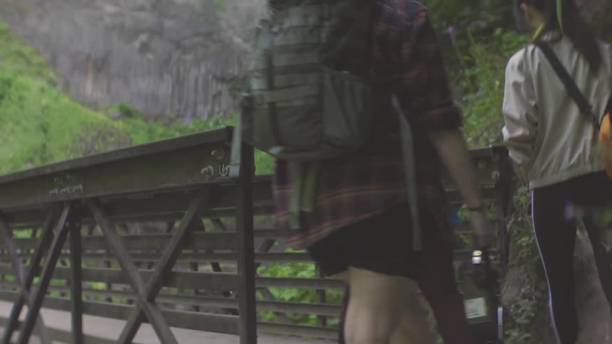 Three women walking and crossing a bridge in a setting with a waterfall in the background