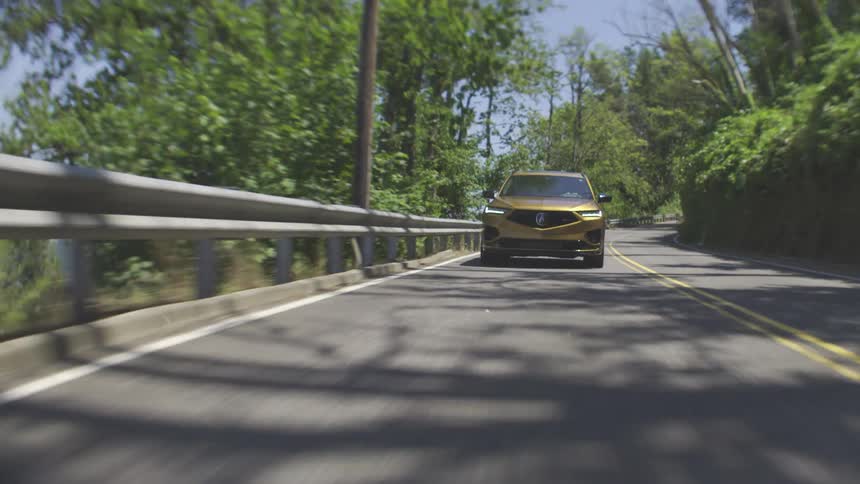 A goldcolored car driving on a freeway with a guardrail alongside the road