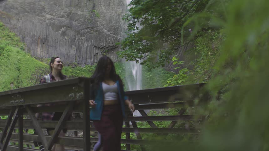 Girls hiking across bridge next to a waterfall in the canyon