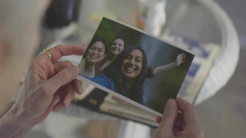 A woman picks a photo from an album containing pictures of three young women examines it then puts it back