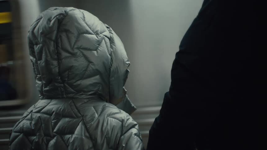 A kid wearing a winter jacket stands at a train terminal watching a passing train