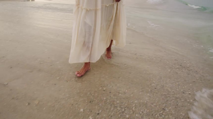 Barefoot woman in dress walking on the beach