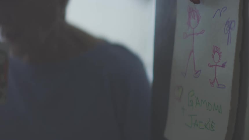 A person drinks beside a wall decorated with kids drawings