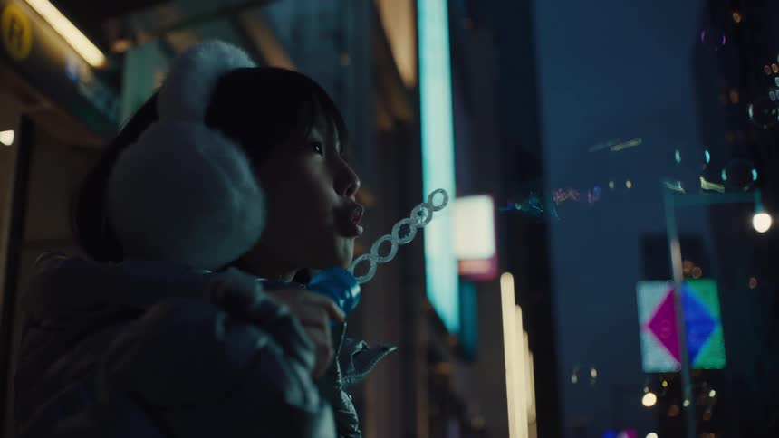 Little girl blowing soap bubbles outdoors in the city at night
