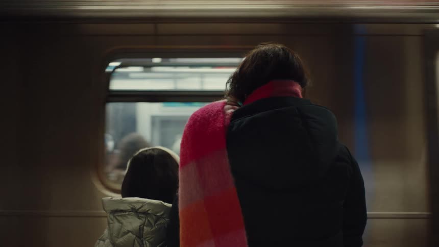 A woman and a child wearing winter jackets standing in a train station waiting to board a train