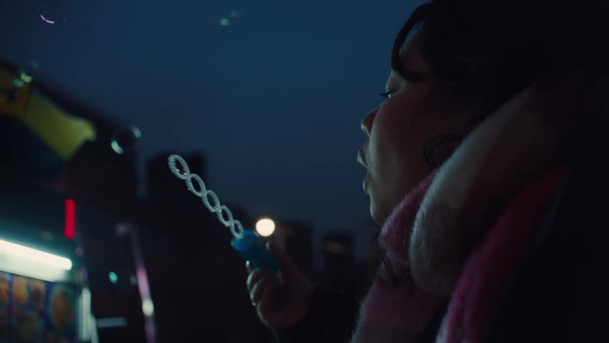 A child bundled in a scarf blows bubbles into the cool night air