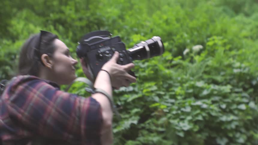 Three women walking in nature with one of them taking photos using a professional camera