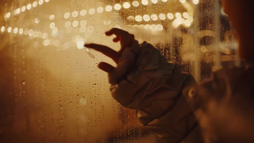 Close up of a young woman drawing a heart symbol on a foggy glass in a play area at night