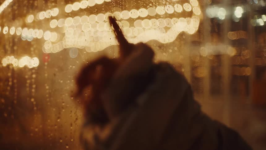 A child draws a heart on a foggy glass window using finger