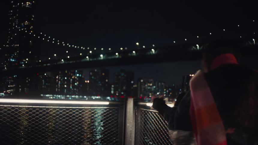 Woman and a child playing in a seaside setting with an illuminated bridge and a city in the background