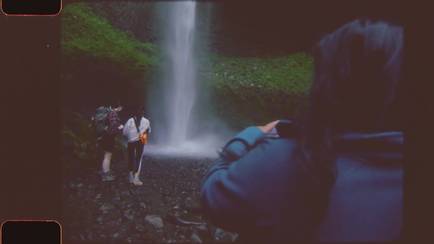 Woman photographing her two other friends taking a picture at a waterfall