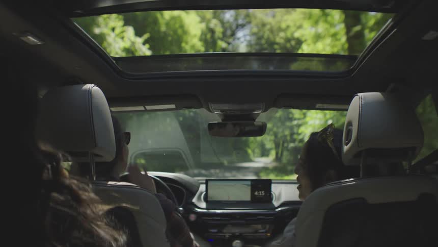 Three women inside a car one is driving and talking while the others are laughing and dancing