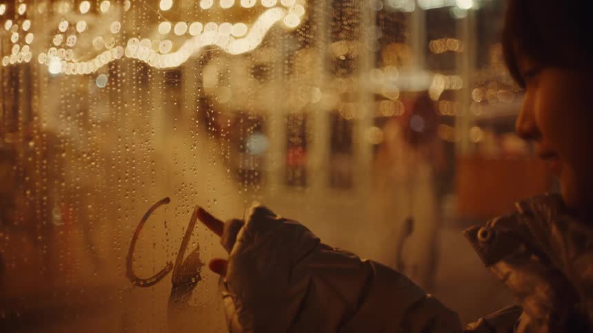 Girl blowing on a glass window and fogging it up and then writing