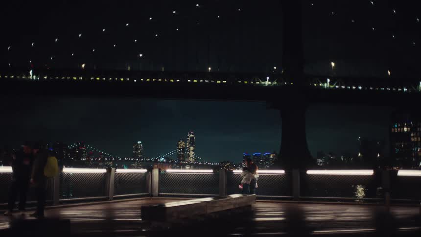 People in a waterfront area of a city with a bridge lit up at night