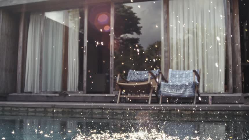 Splashing water in a pool with chairs in the background at a house