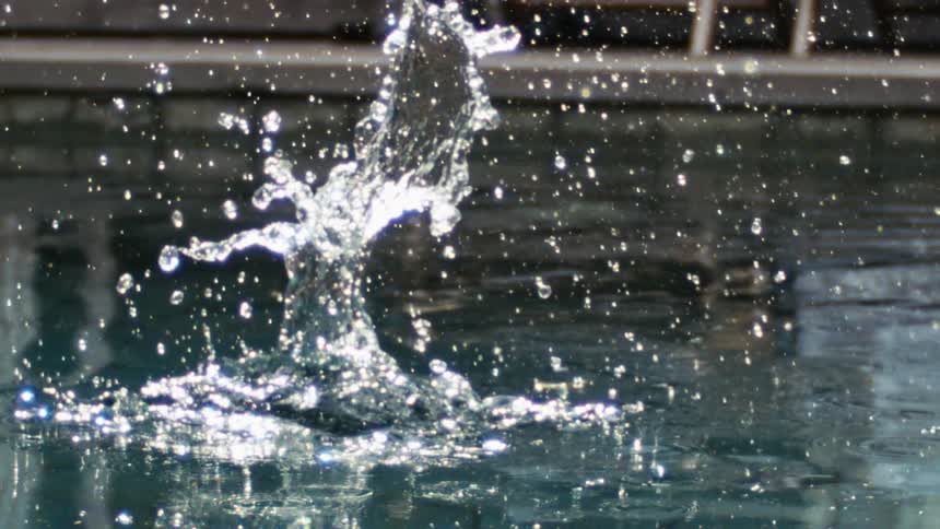 An outdoor pool splashes as a piece of rock is thrown into it