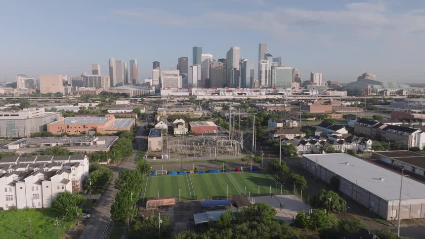 The video shows an aerial view of a city with a skyline of tall buildings in the foreground there are lowerlying buildings including an industrial area and some residential townhouses the video appears to be filmed in houston texas
