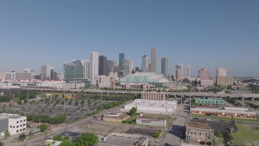 An aerial shot of a city skyline with many tall buildings the city is surrounded by highways and parking lots and the sky is clear and blue